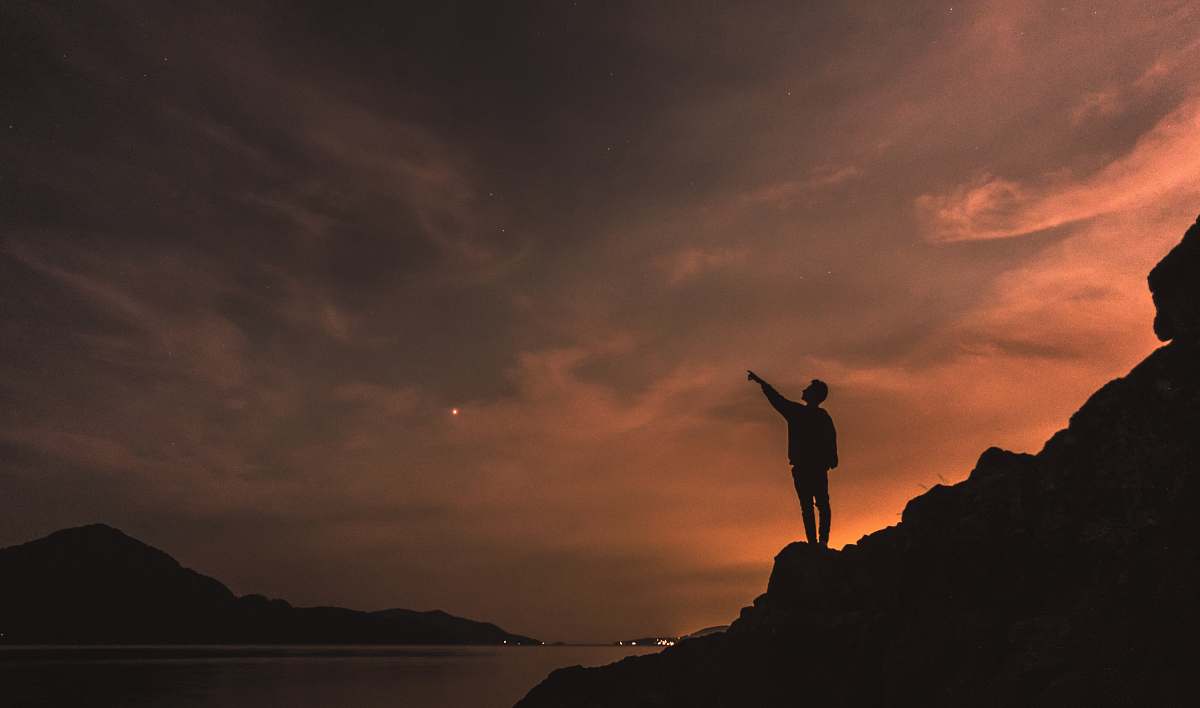 human silhouette photography of person standing on rock beside body of water outdoors