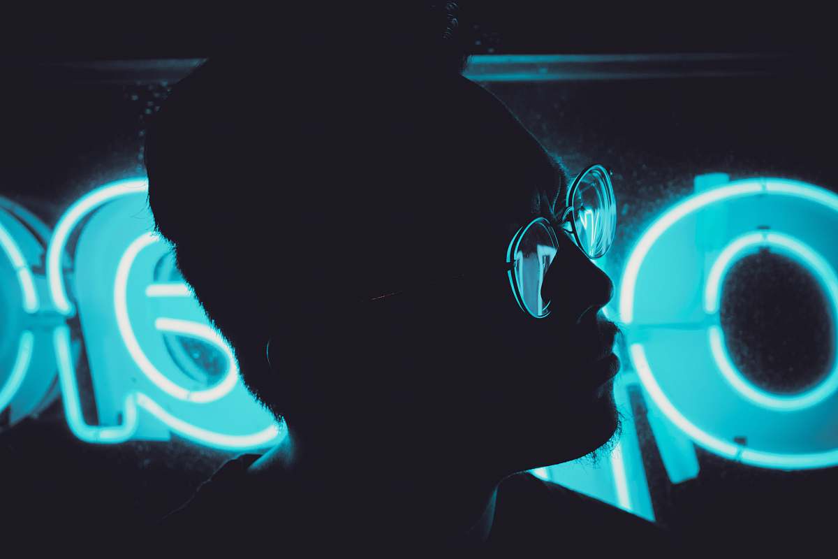 light man wearing sunglasses beside LED sign portrait