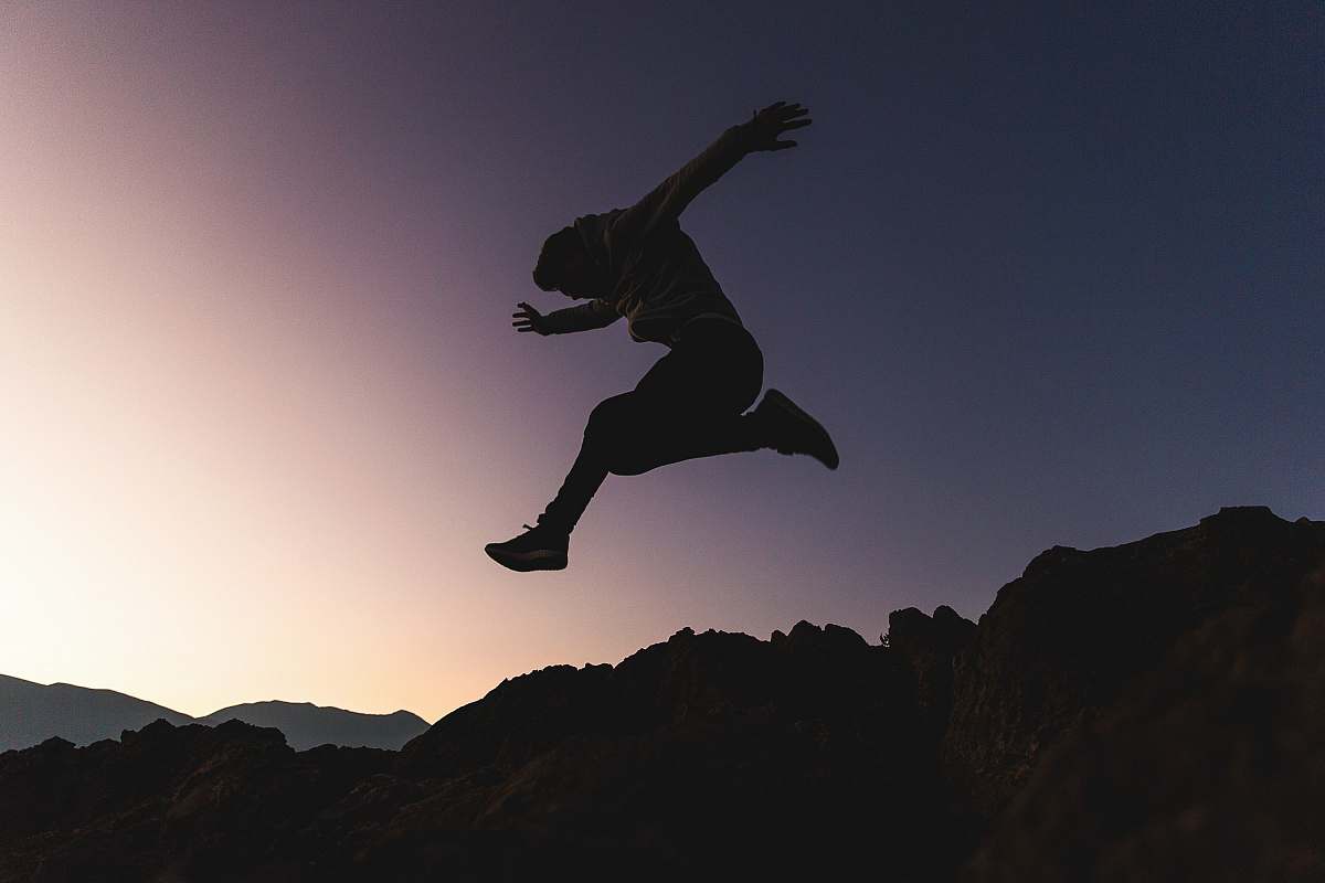 silhouette man jumping above mountains adventure