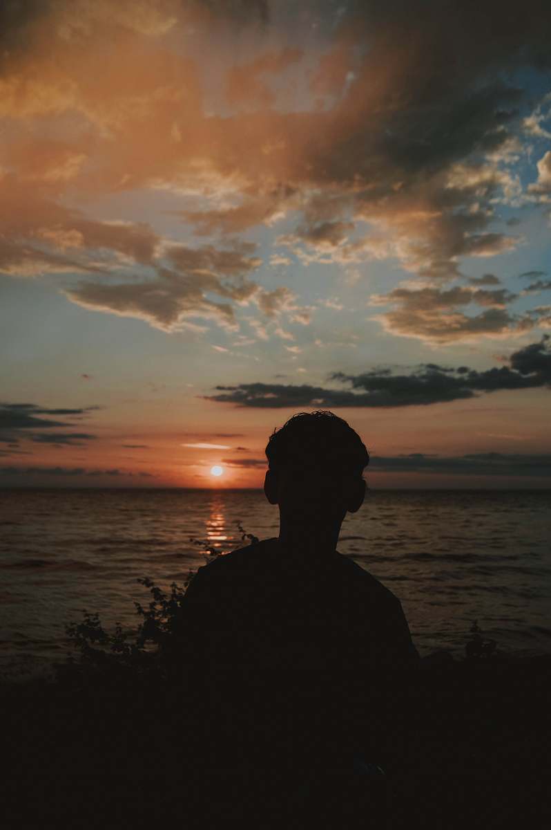 nature silhouette photography of person standing beside body of water sunset