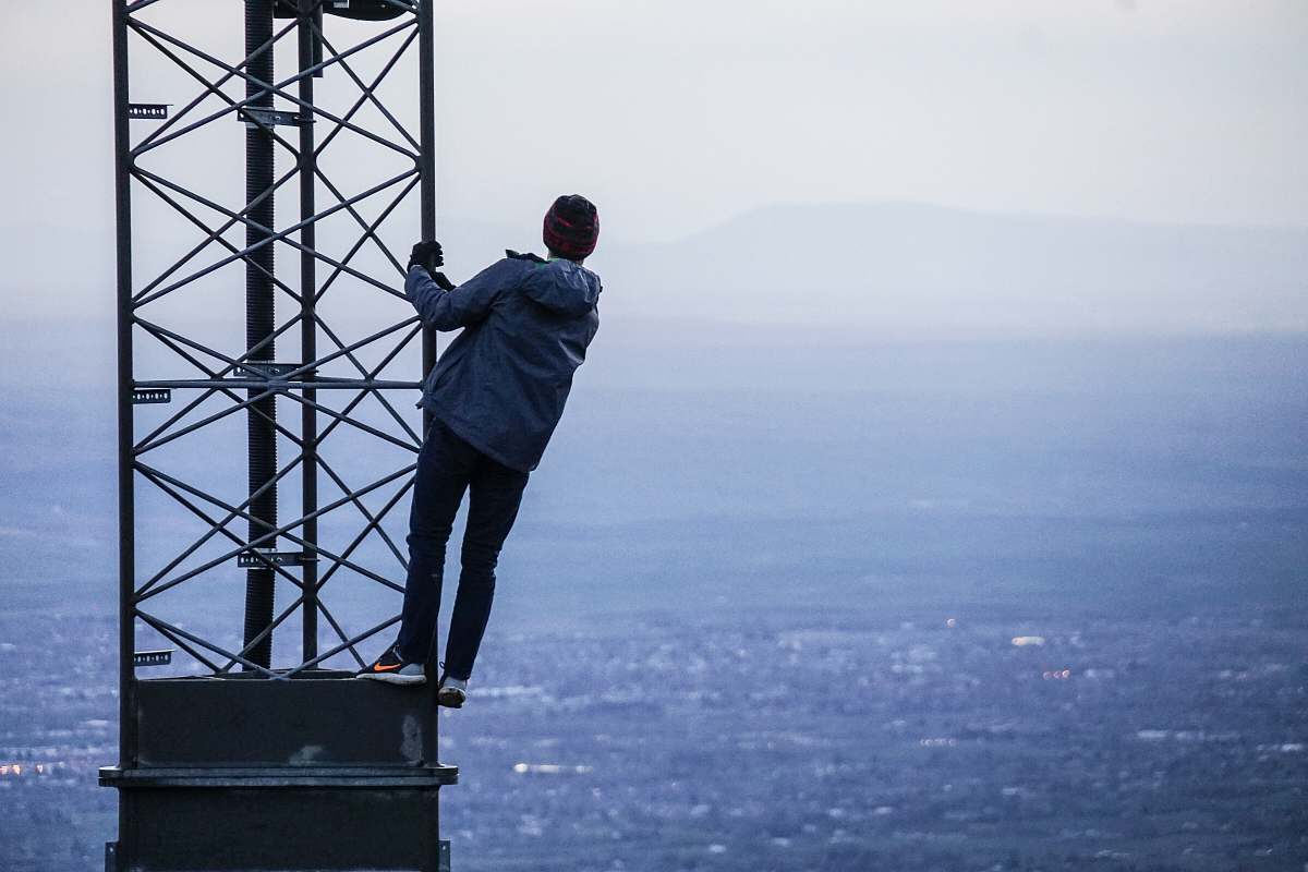 person man climbing on tower near buildings at daytime human
