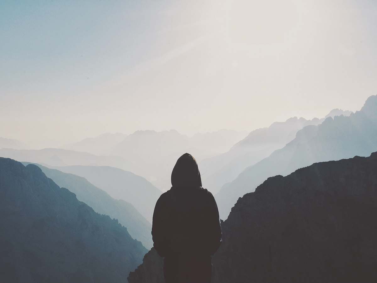 grey man in hoodie standing in front of the mountain person