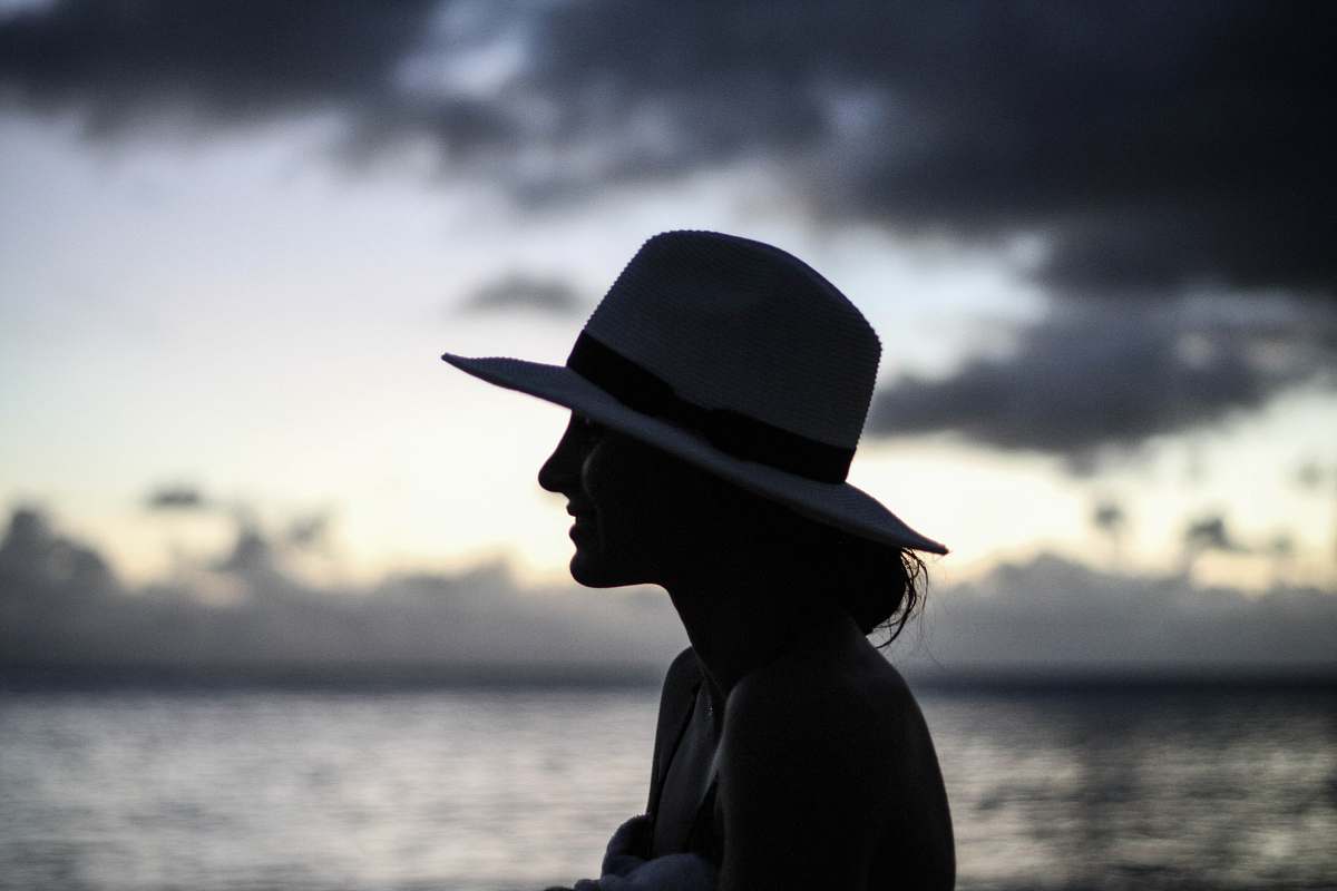 hat silhouette of woman standing beside body of water cowboy hat