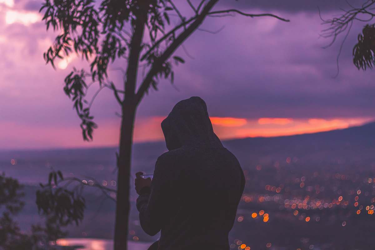 person silhouette photo of man standing at the peak facing cityscape human