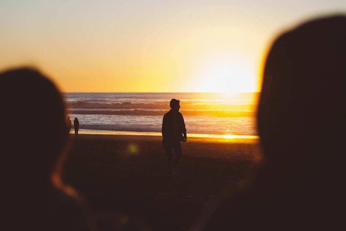 waves silhouette photo of man standing near seashore at sunset ocean