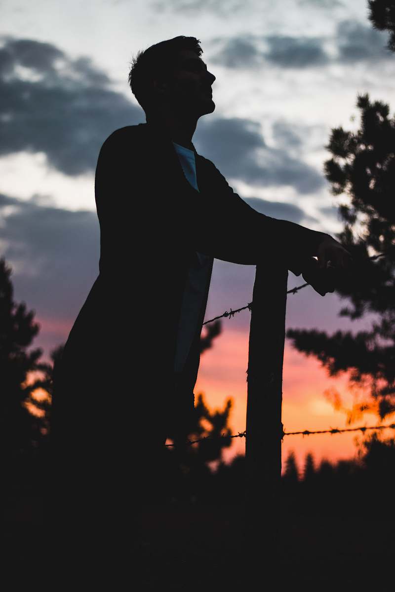 human silhouette photography of man standing beside barbwire person