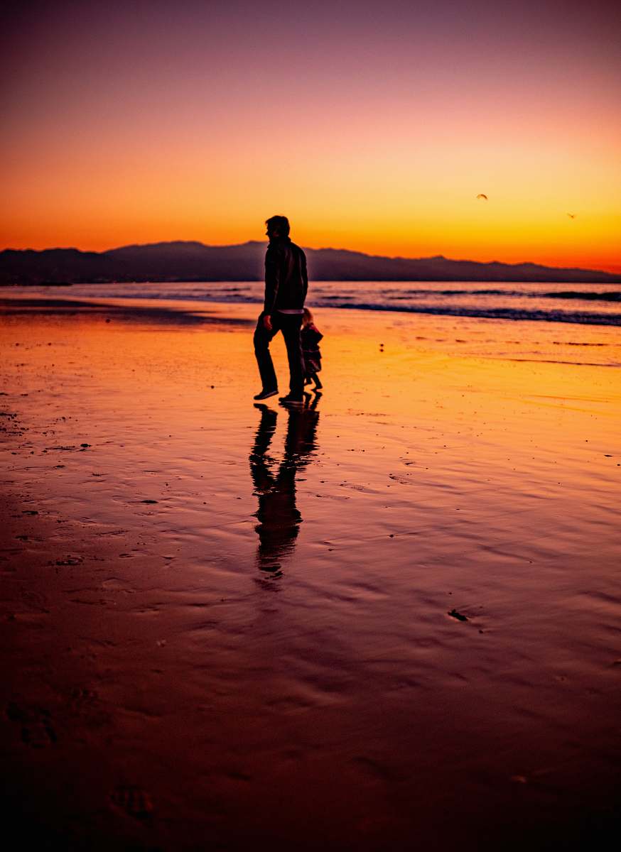 human man and child walk at the seashore during sunset standing
