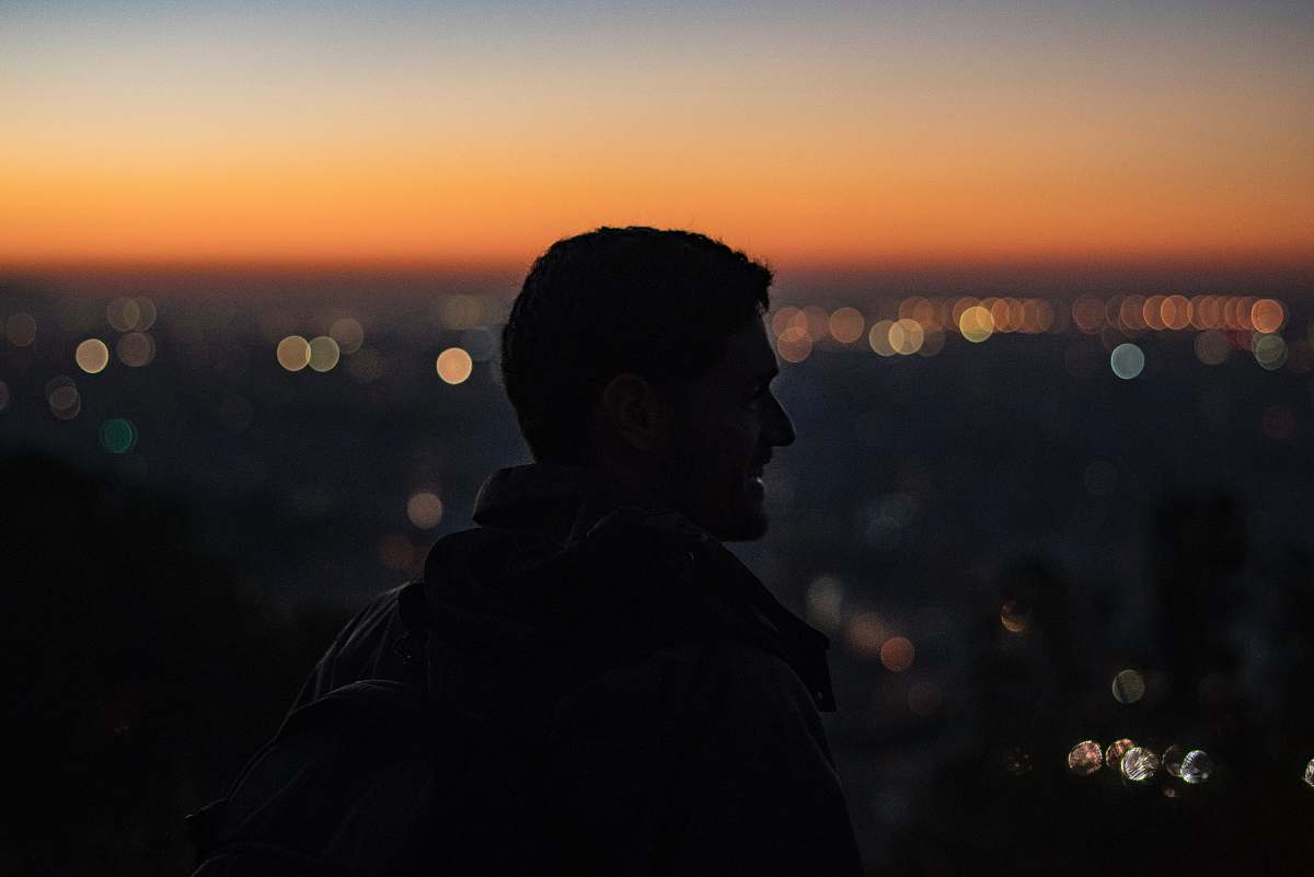 human man on high ground facing right looking at city during nighttime people
