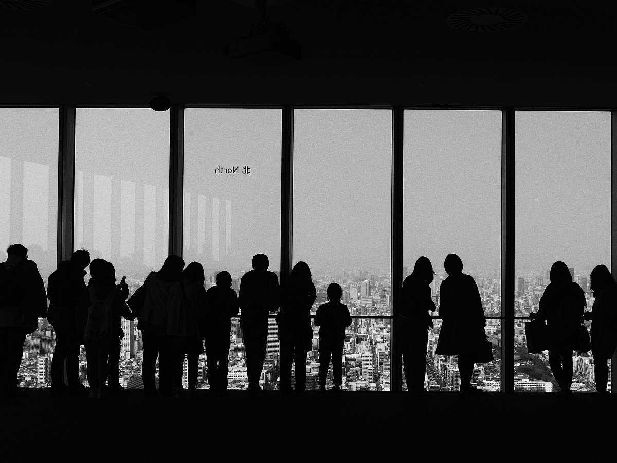 human people overlooking buildings inside room black-and-white
