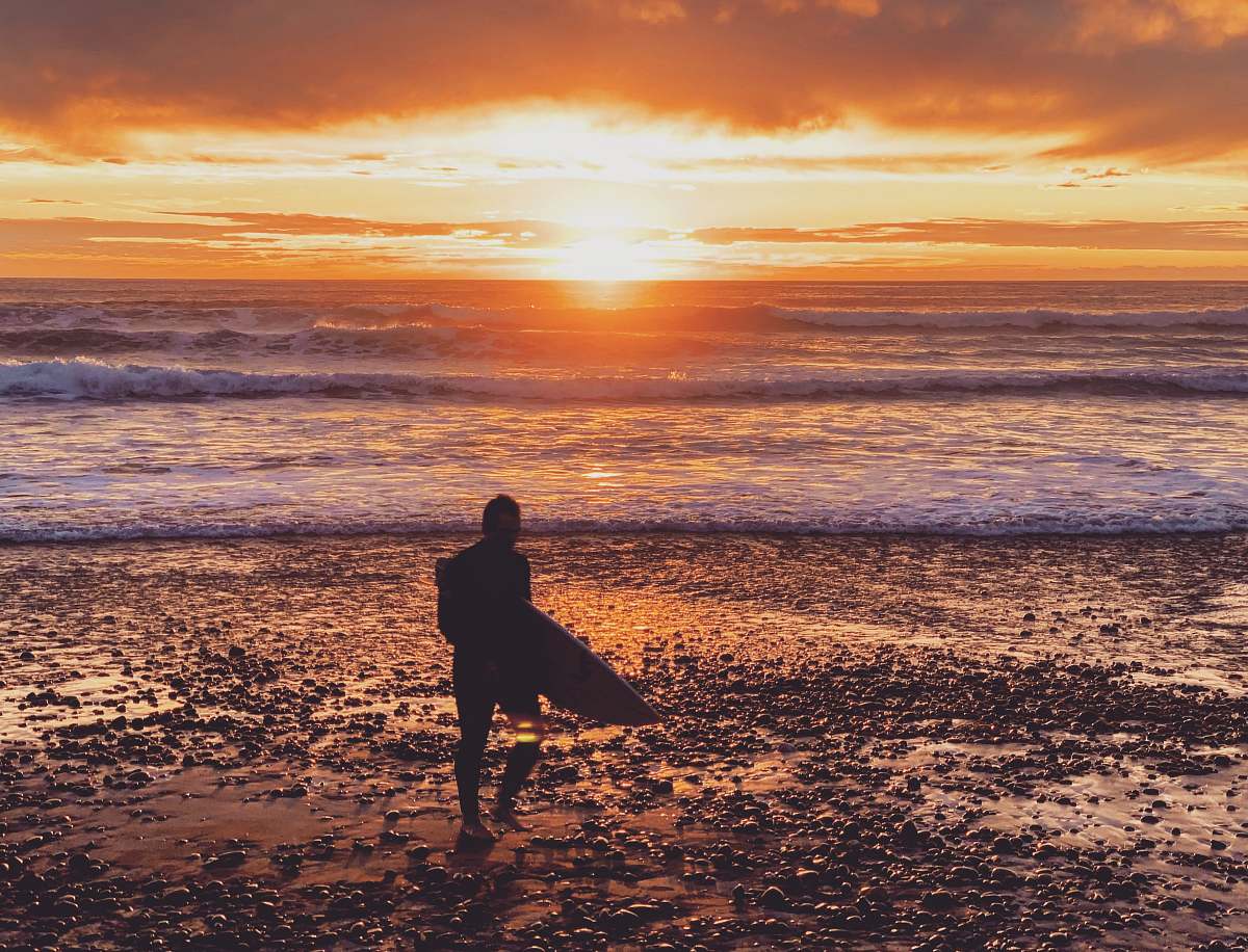 human person holding surfing board walking towards sea during sunset standing