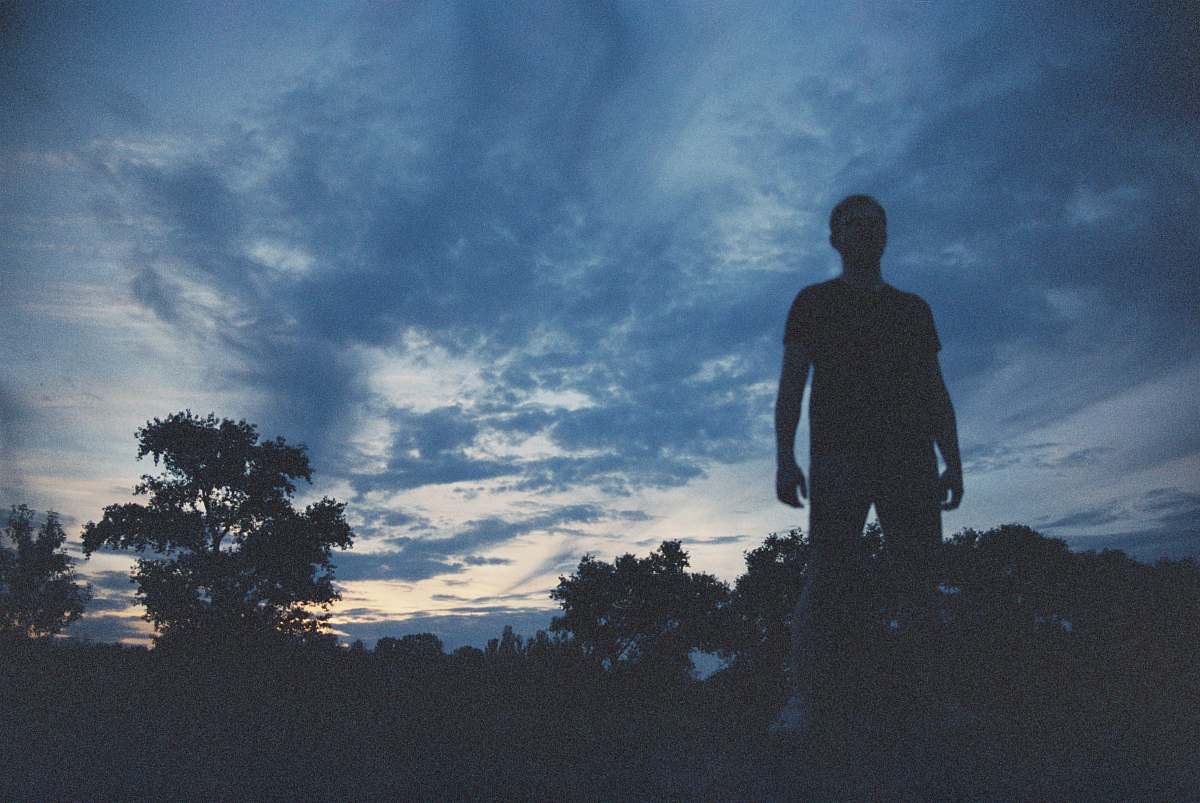 silhouette person standing near high trees during golden hour human