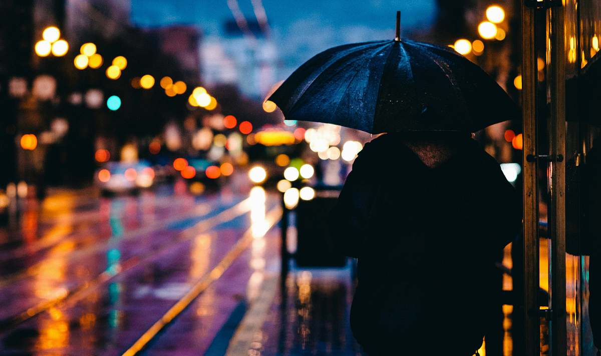 city person walking on street while holding black umbrella near cars on road at nighttime rain