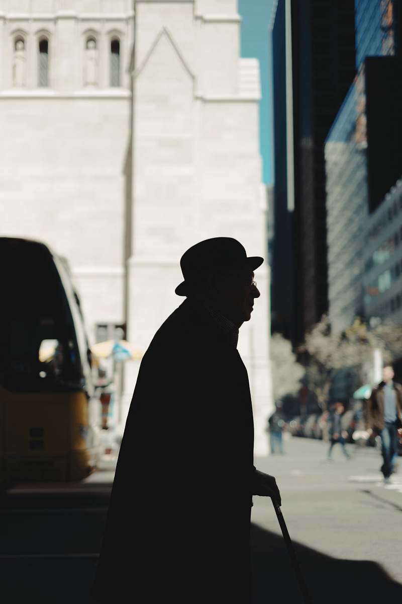 human silhouette of man holding walking cane on road during daytime people