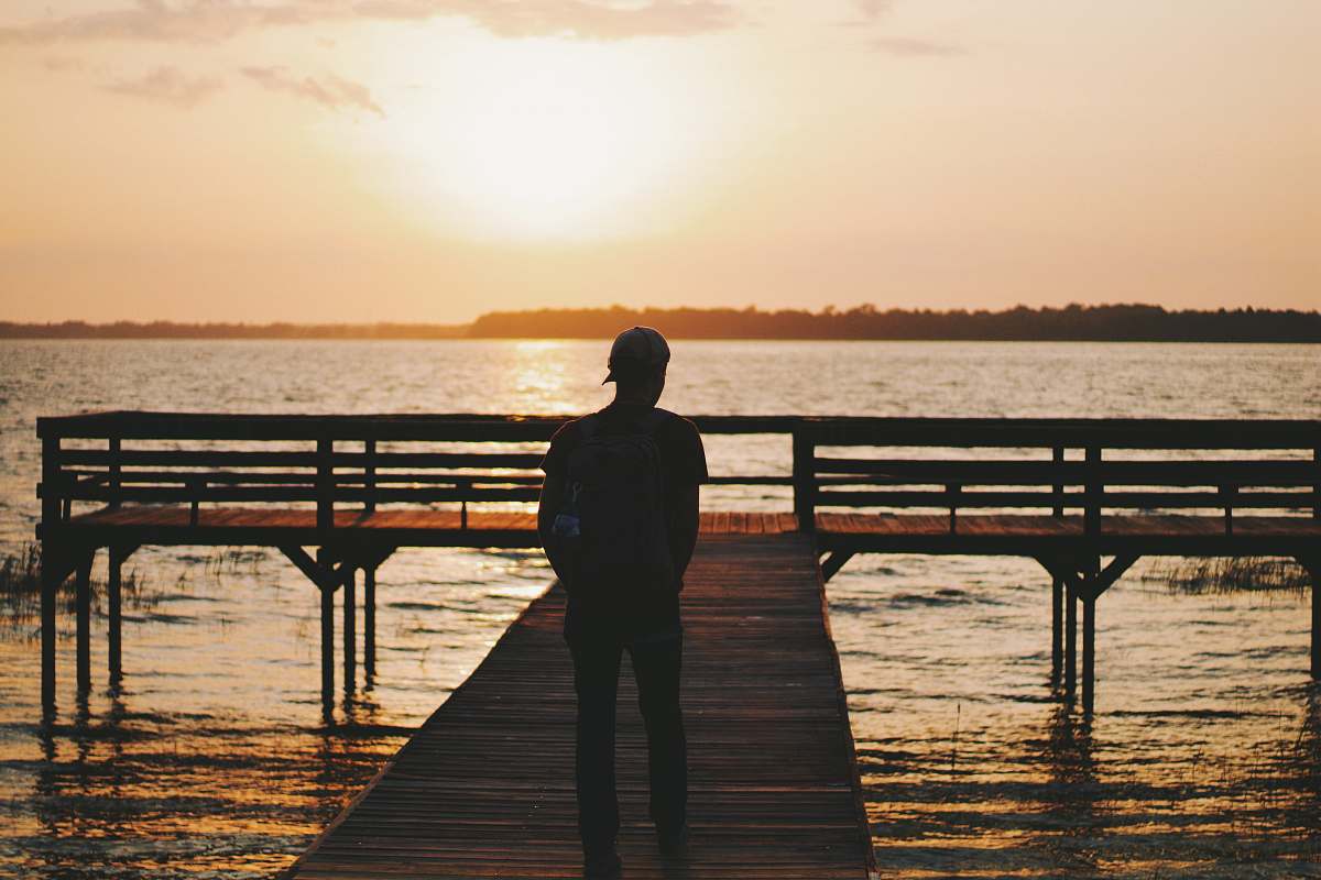 people silhouette of man walking on dock during golden hour water