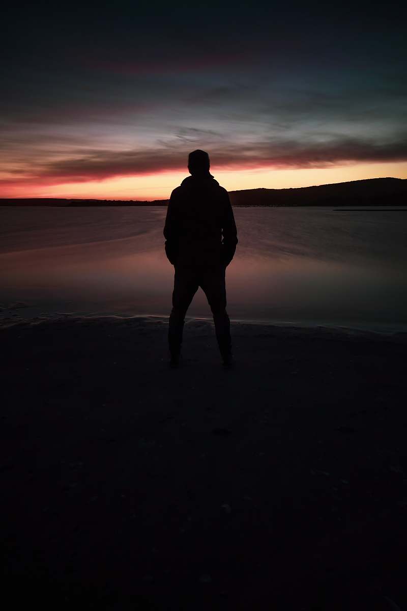 human silhouette of person standing and facing on calm sea during golden hour standing