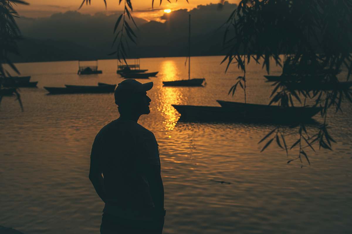 human silhouette of person standing near body of water and boats on body of water nature