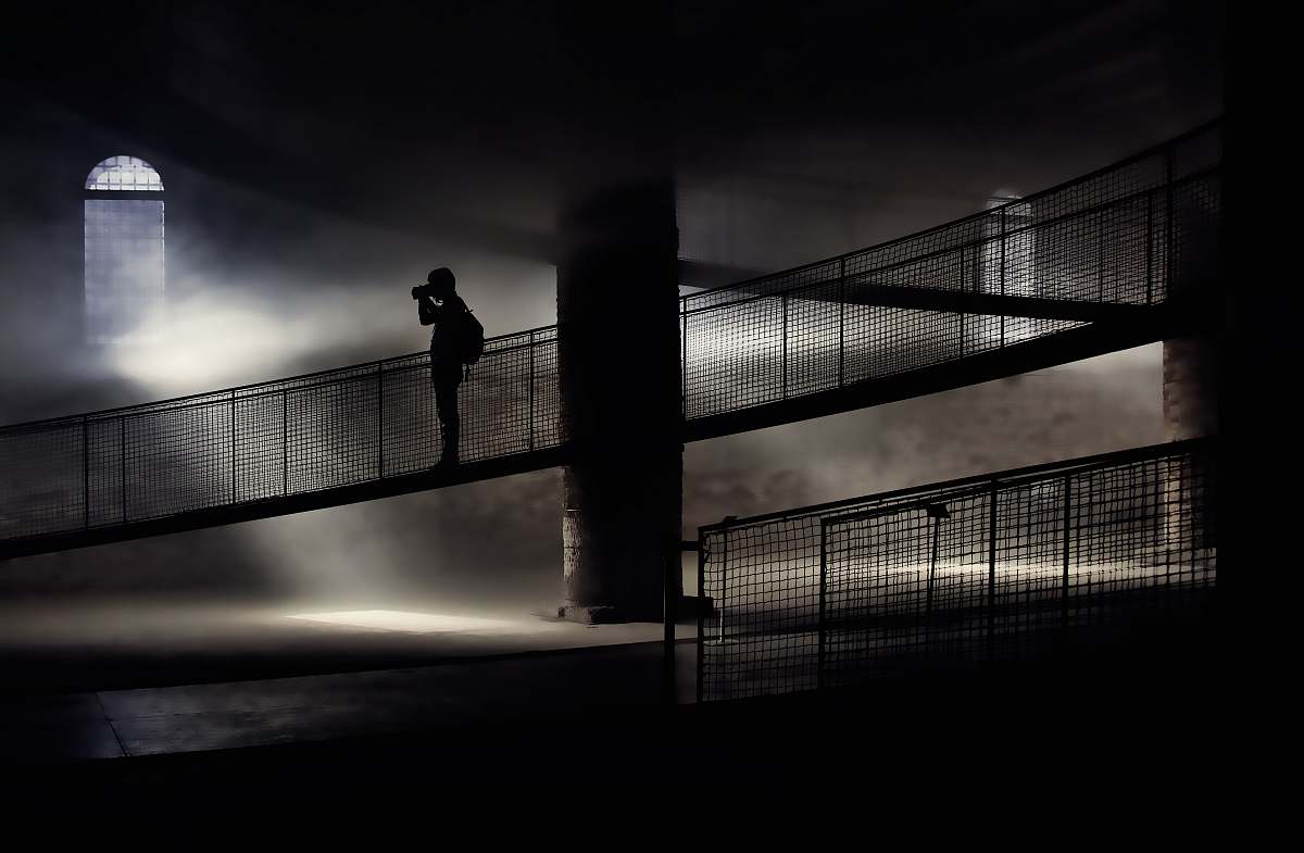 light silhouette of person standing on bridge while taking photo photographer