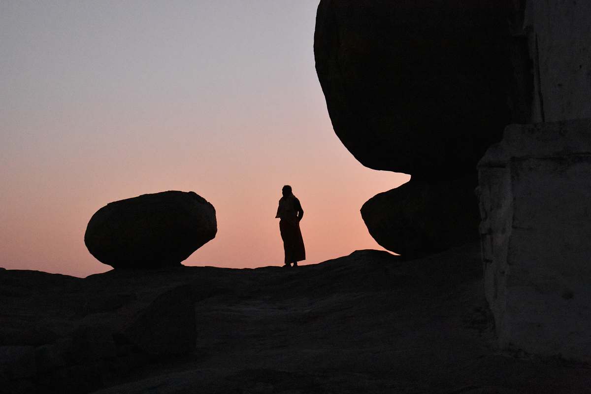 human silhouette of person standing on high ground beside large rock nature