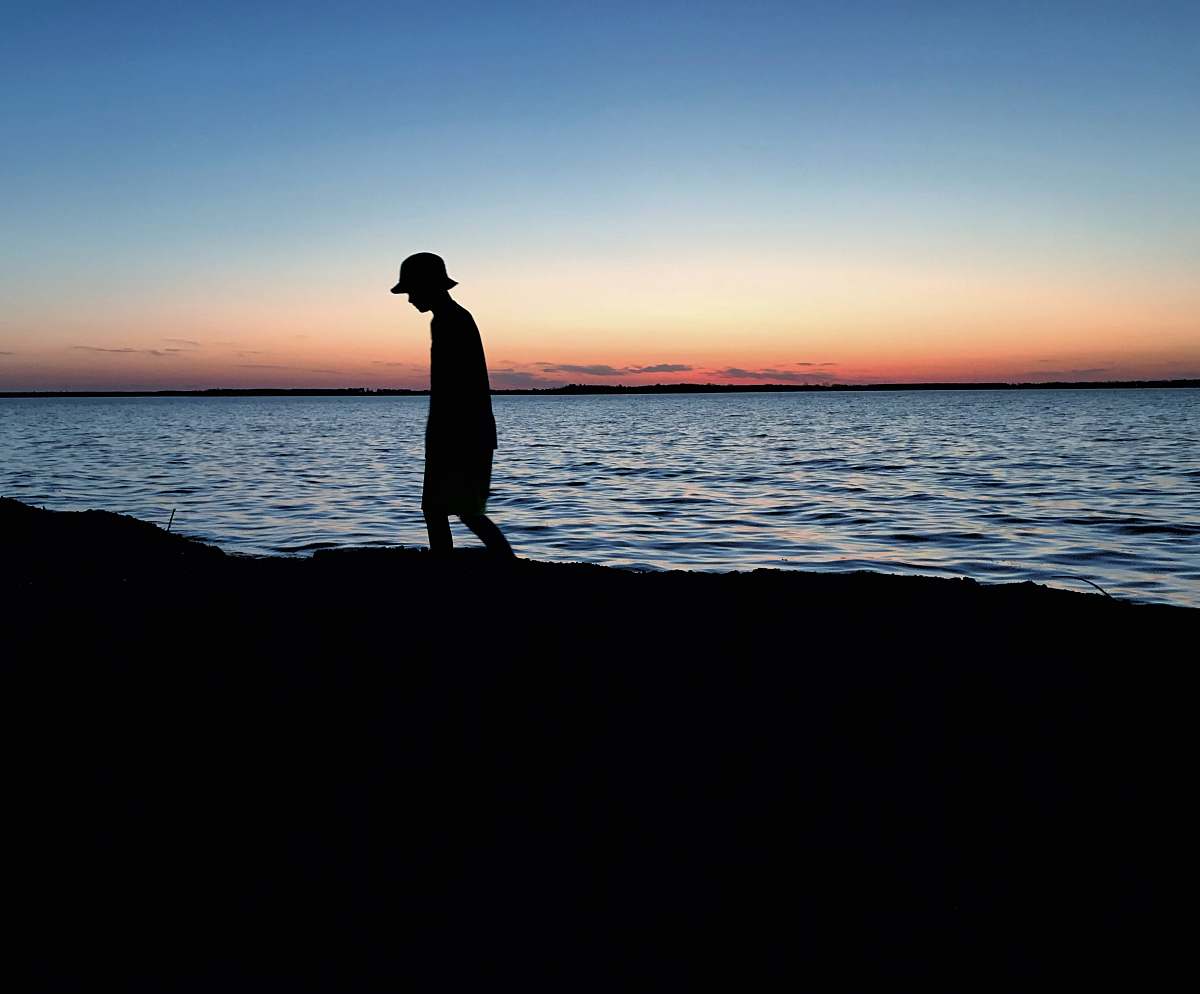 human silhouette of person walking near body of water standing