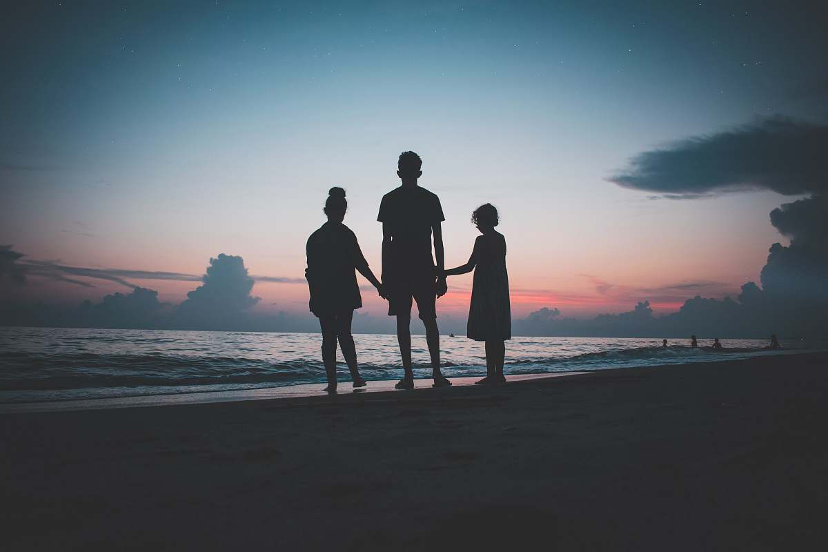 human silhouette of three people walking beside body of water people