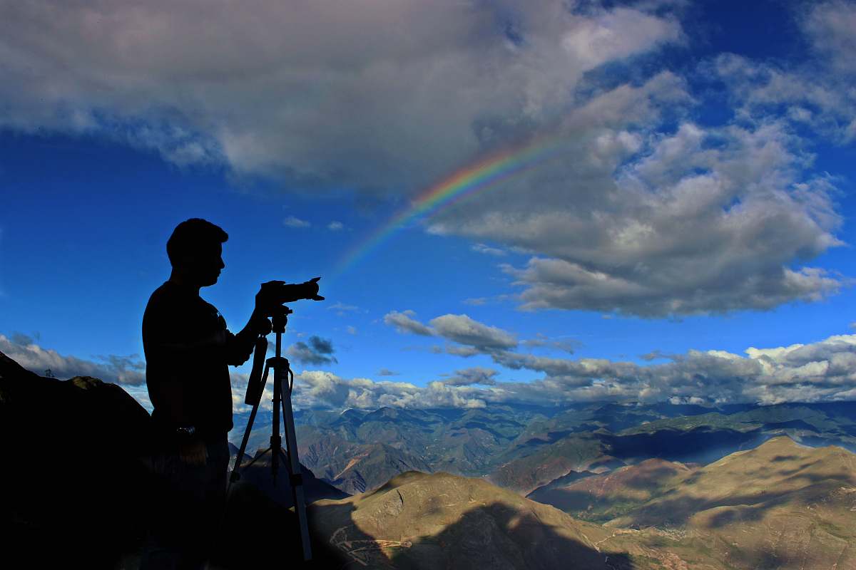nature silhouette photo of holding camera with stand during daytime with rainbow sky