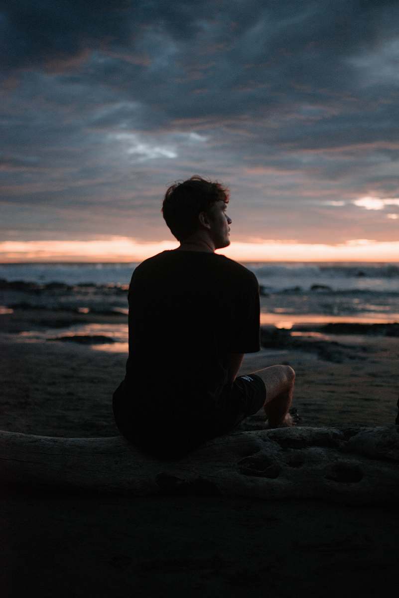 human silhouette photo of man sitting on beach silhouette