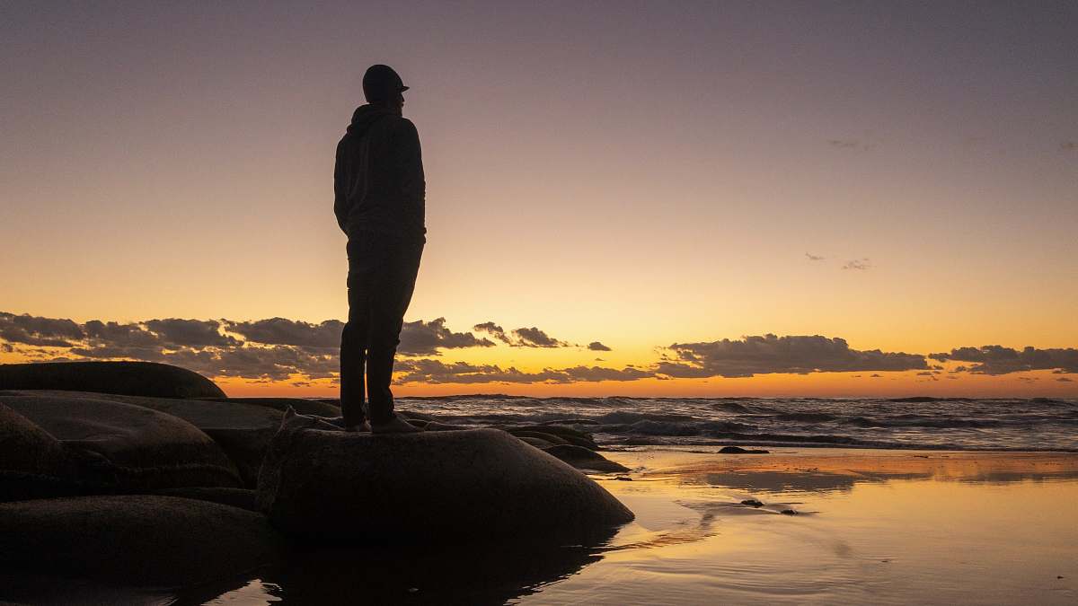 human silhouette photo of man standing on stone standing