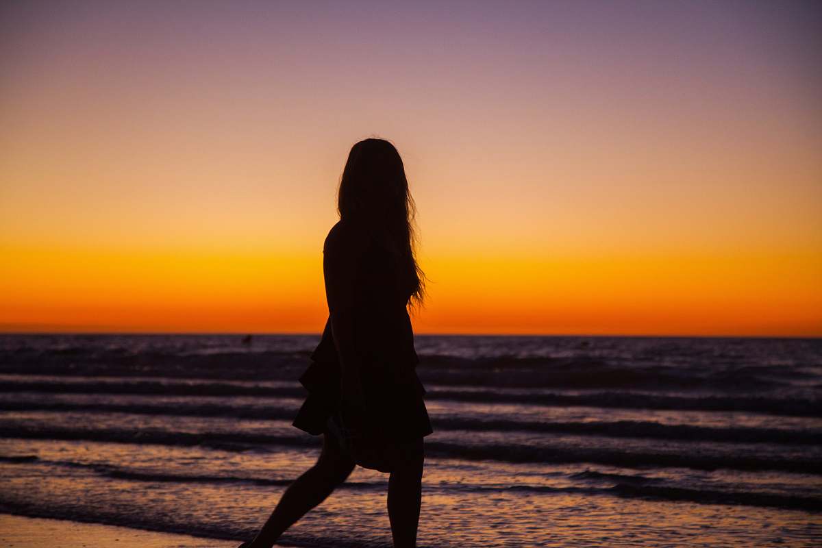 human silhouette photography of woman walking on seashore standing
