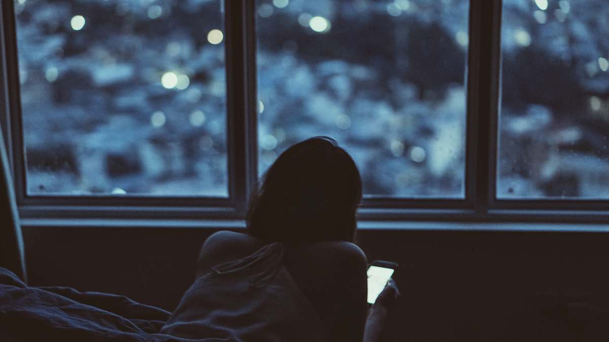 window woman holding phone near window during daytime back