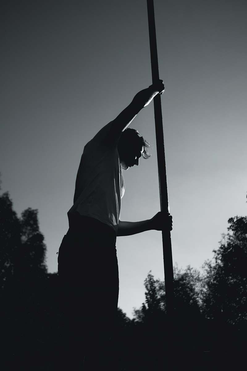 man man in white shirt holding pole grey