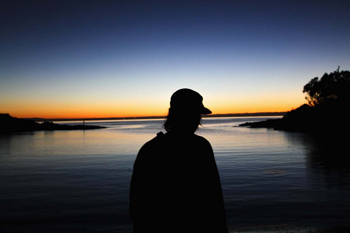person man standing near body of water silhouette photography sunrise
