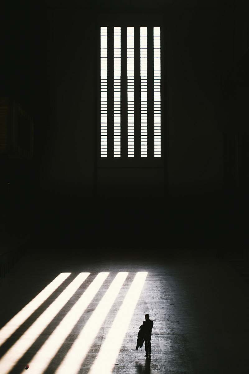 prison man standing near window with window blinds grayscale photography black