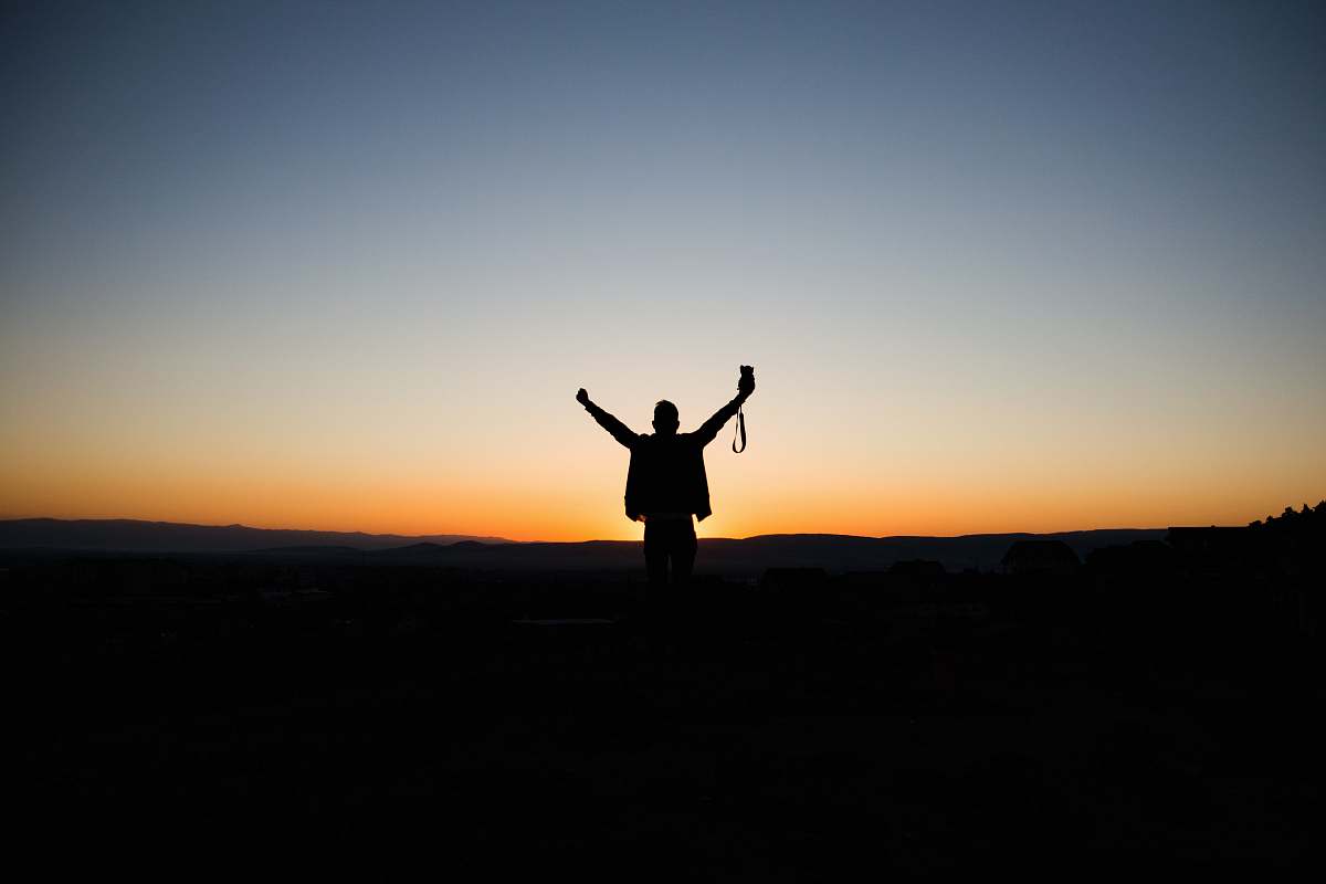 nature man stretching his arms silhouette at sunrise outdoors