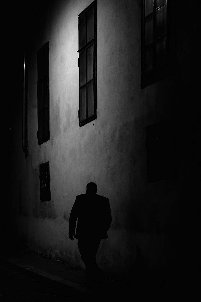 person man walking beside gray concrete wall during night time black-and-white