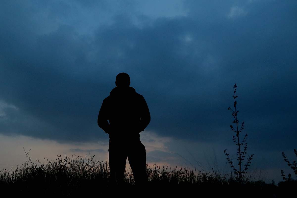 human person standing and facing back on green field under blue and white sky person