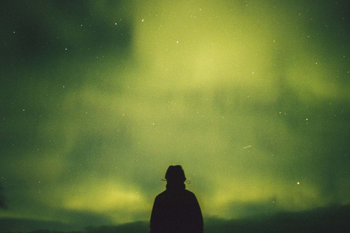 human person standing under green aurora borealis person