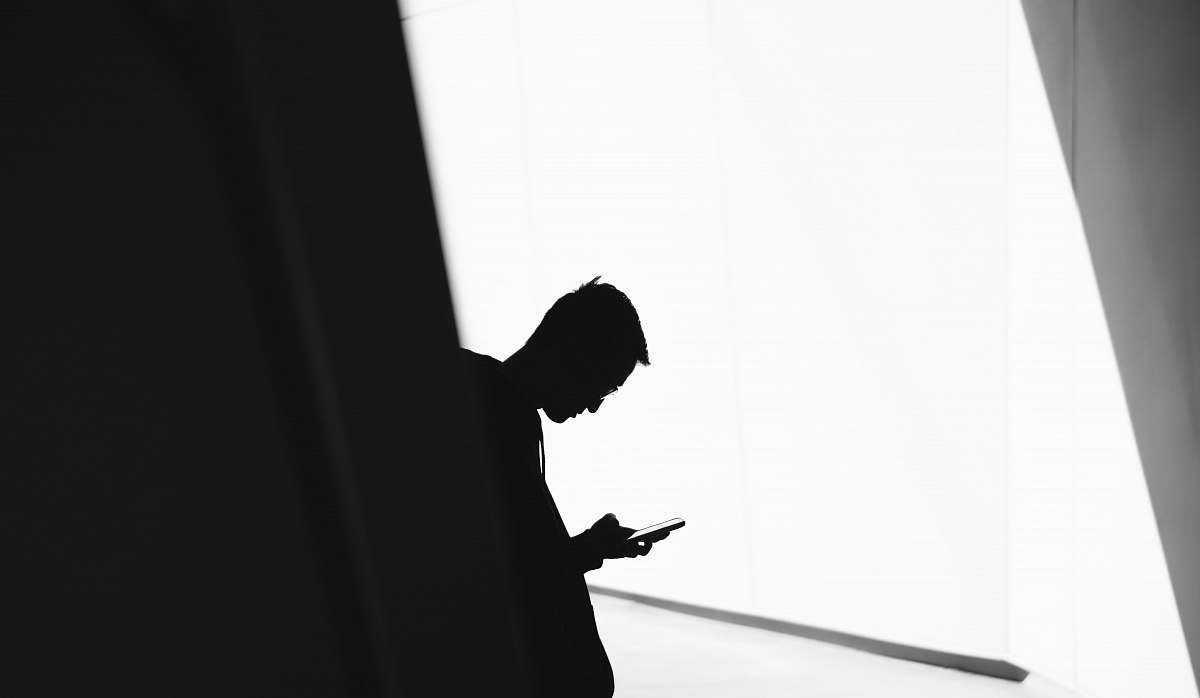 person person using phone leaning on wall in silhouette photography black-and-white