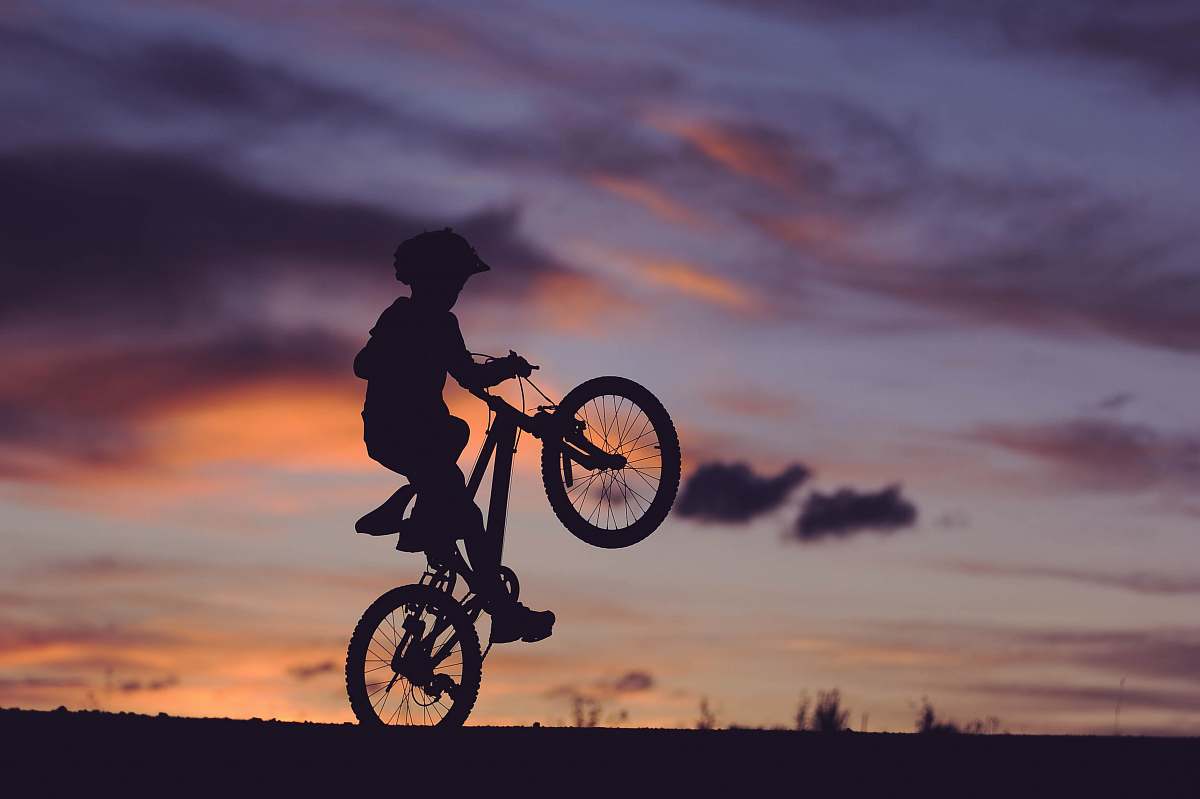human silhouette of boy riding bicycle in wheelie during golden hour person