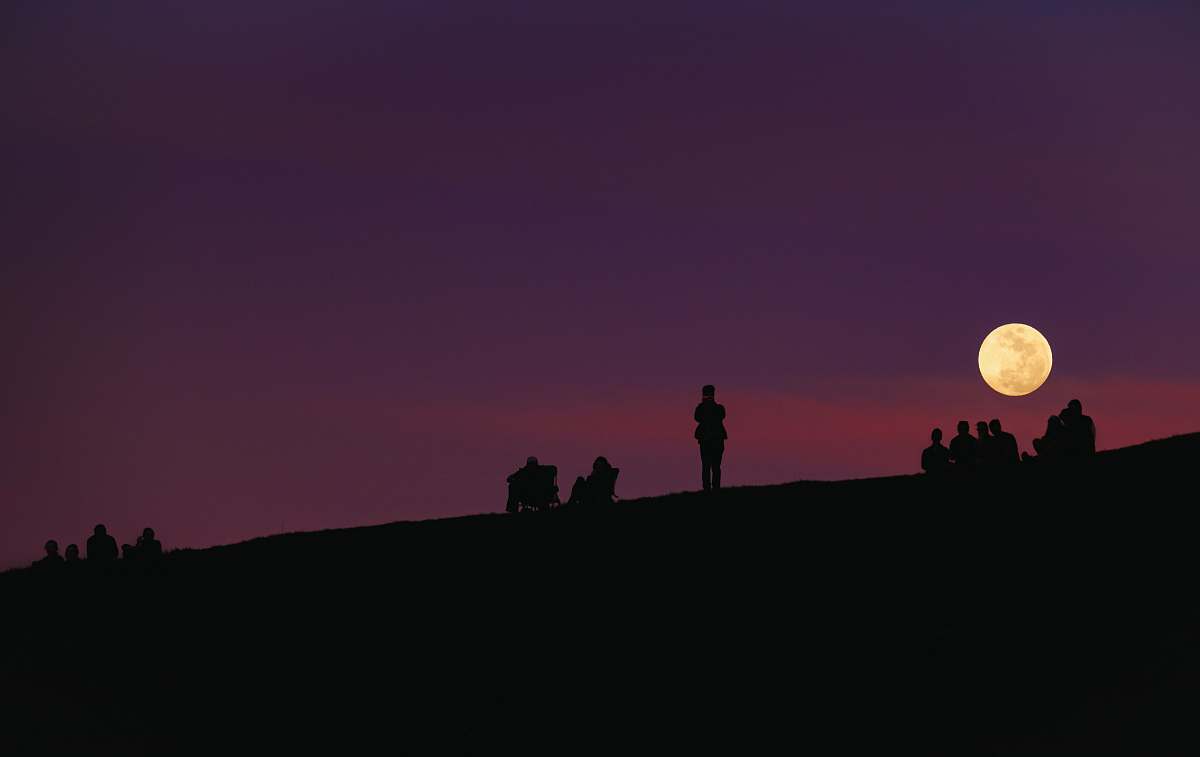 moon silhouette of group of people under purple night sky full moon