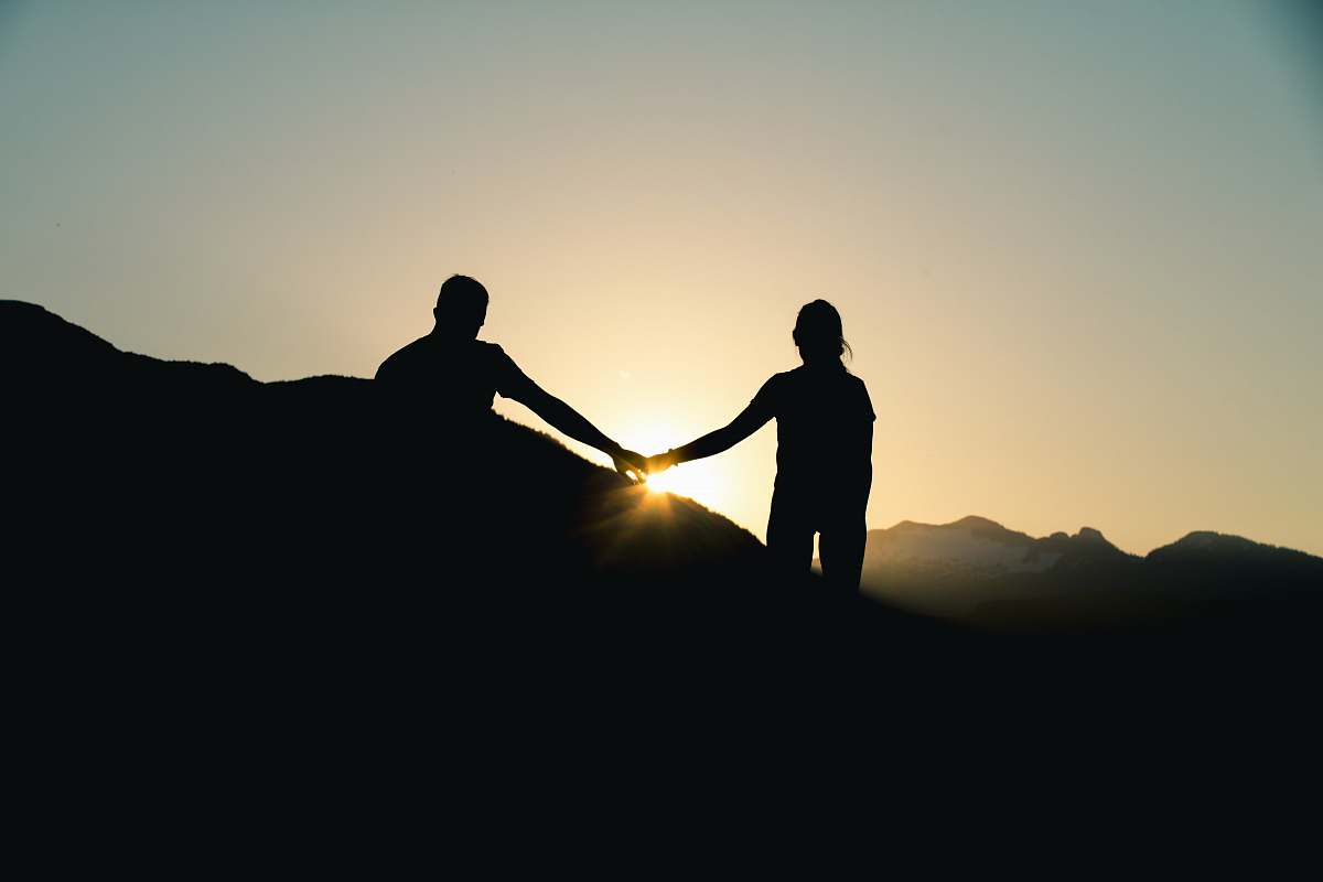 person silhouette of man and woman holding hands while walking under gray sky during daytime people