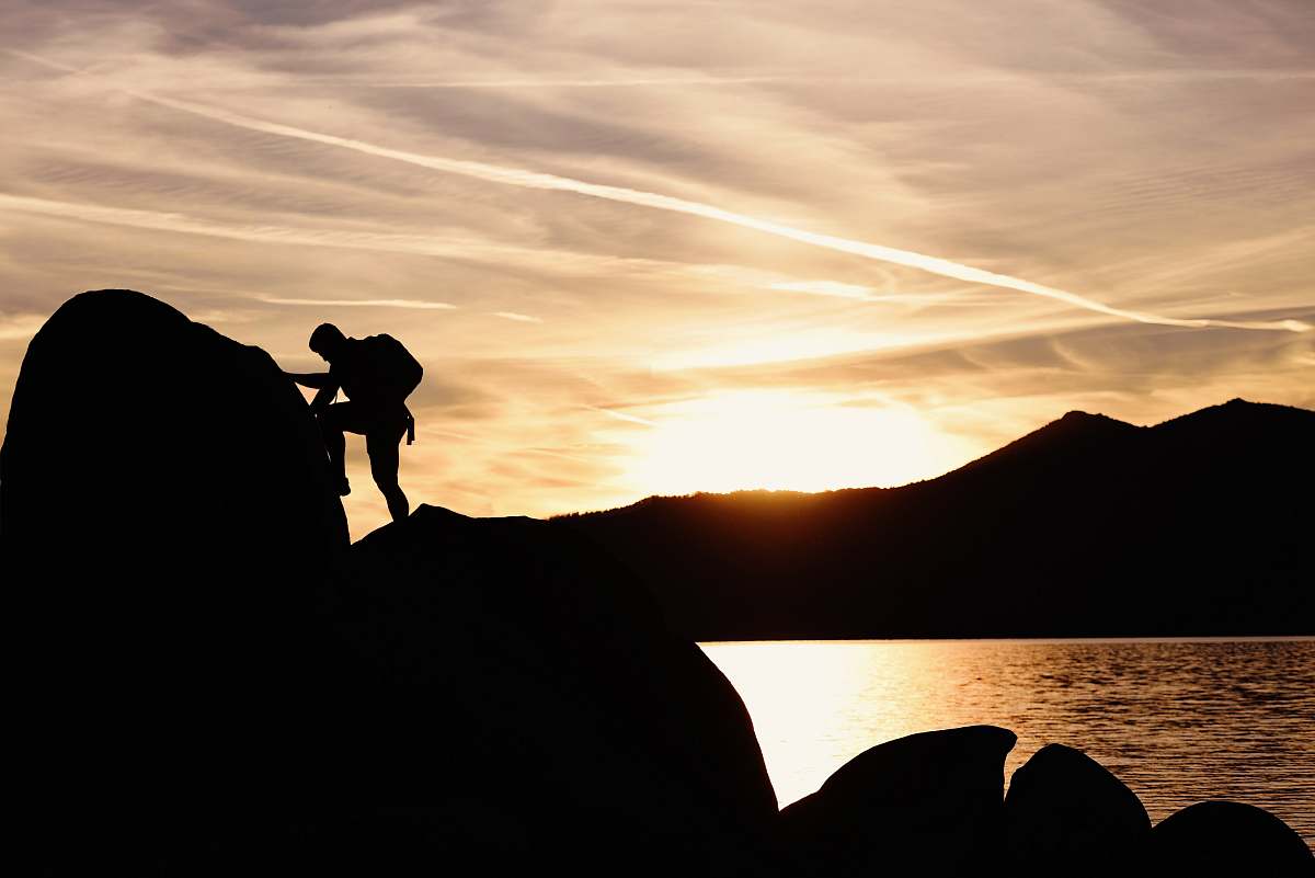 human silhouette of man climbing rock boulder near sea during golden hour outdoors