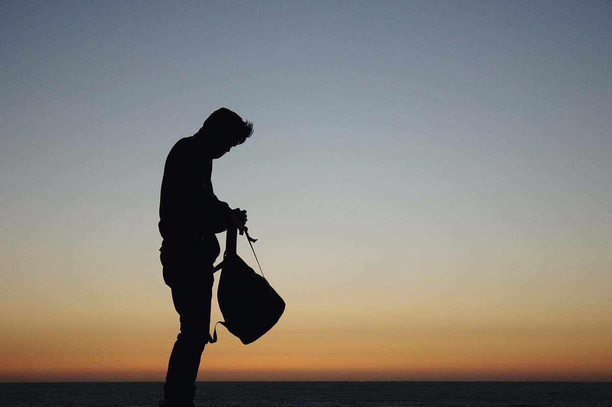 human silhouette of man holding backpack during orange sunset person