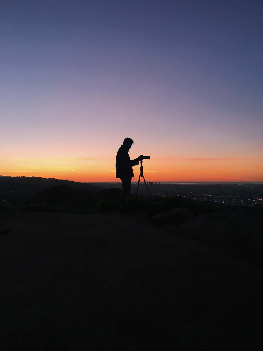 sky silhouette of man in front of DSLR camera during golden hour horizon