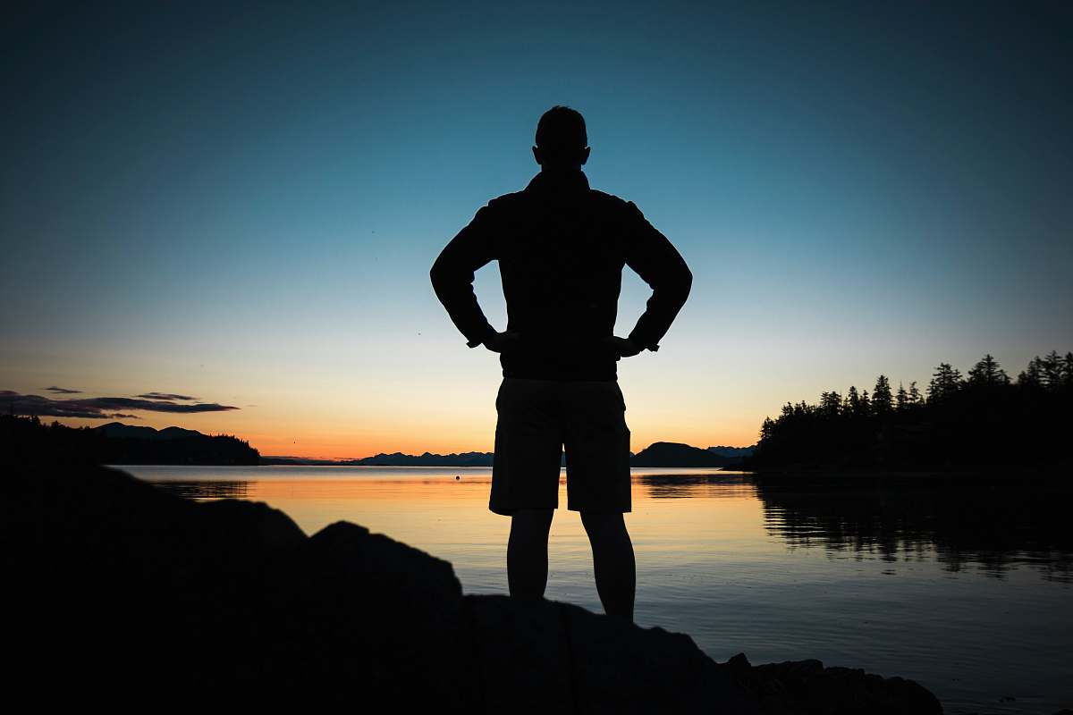 person silhouette of man standing near body of water during golden hour sunset
