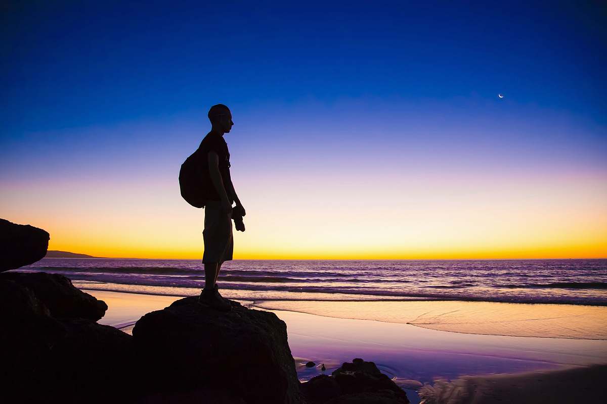 person silhouette of man standing on cliff shore