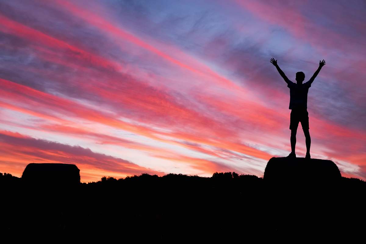 sky silhouette of man standing on high ground under red and blue skies sunset