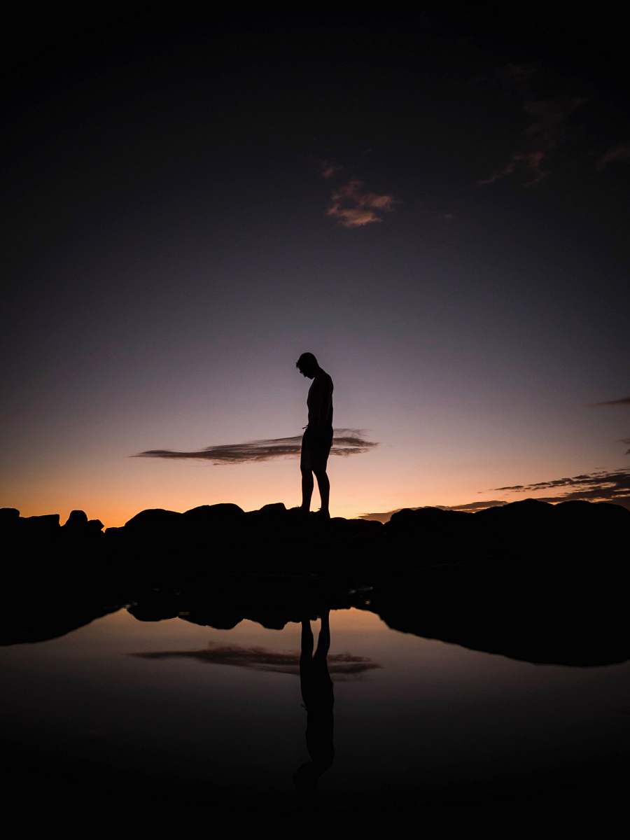human silhouette of man standing on rocks near body of water during sunset standing