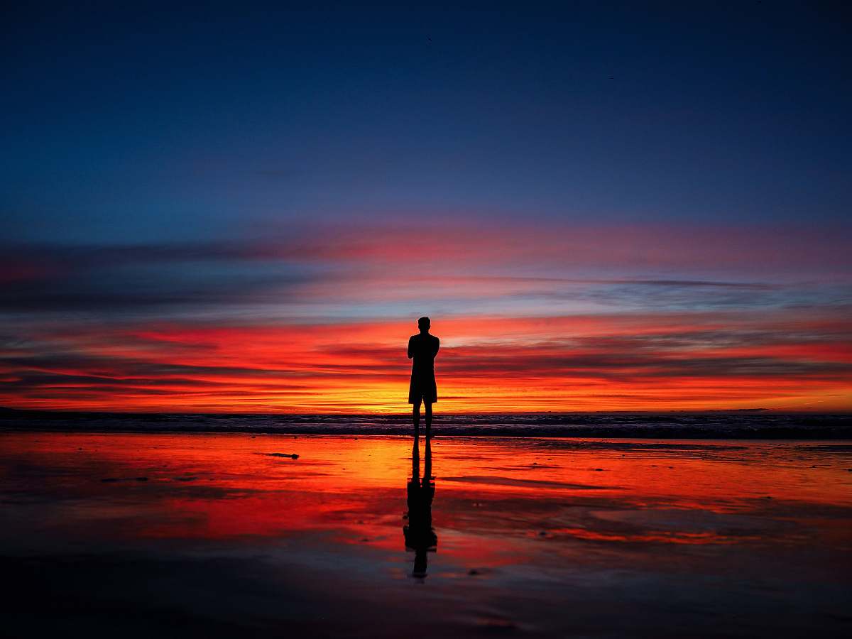 nature silhouette of man standing on shoreline at night time sunset