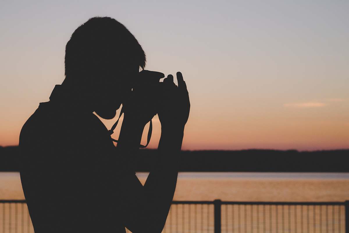 man silhouette of man using camera near balustrade during sunset photographer