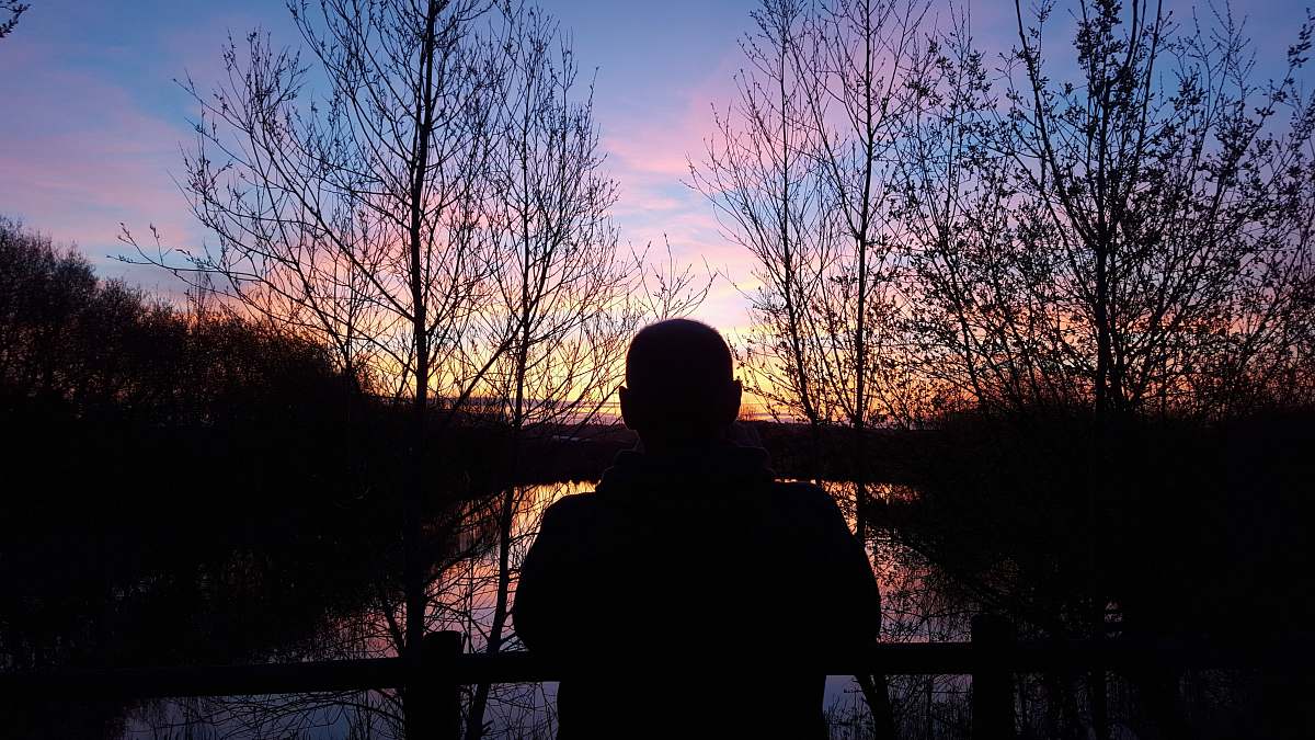 outdoors silhouette of man watching orange setting sun in horizon nature